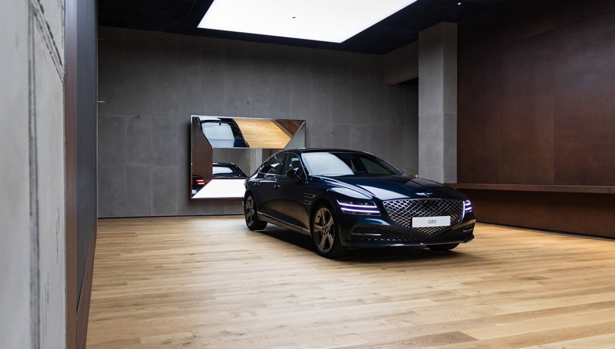 Un studio à atmosphère calme, avec un sol en bois clair, des plafonniers flatteurs et deux voitures étincelantes en exposition.