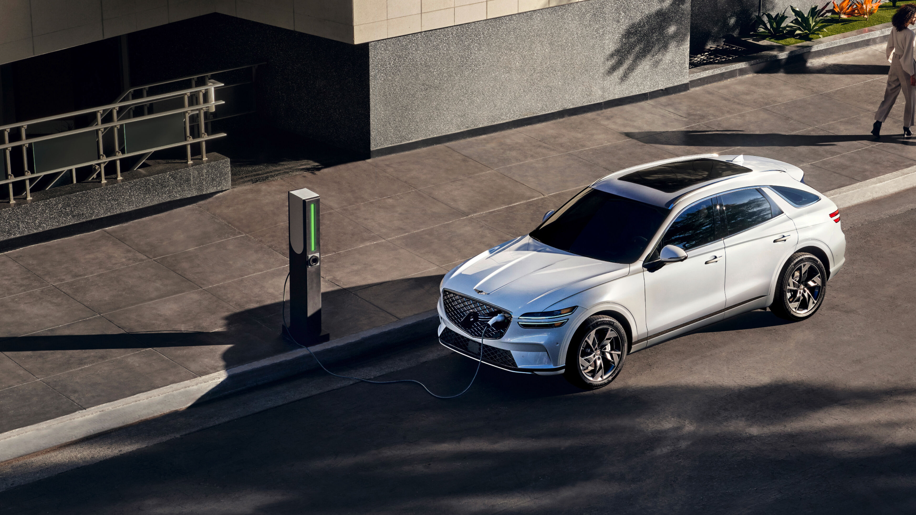 The white Electrified GV70 is parked on a quiet street, electronically charging.