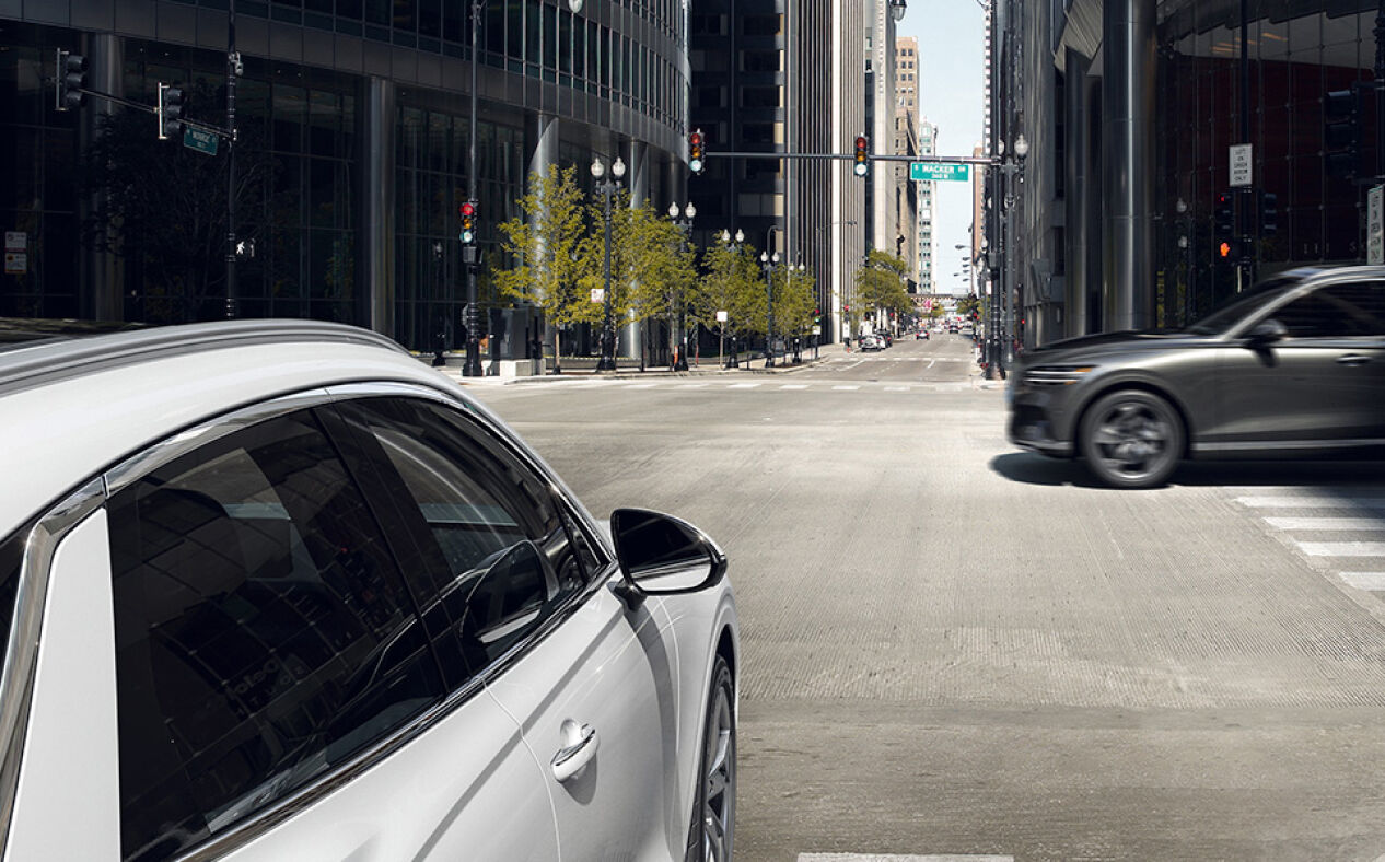 The Electrified GV70 is about to drive through a crossroads as another car speeds across.