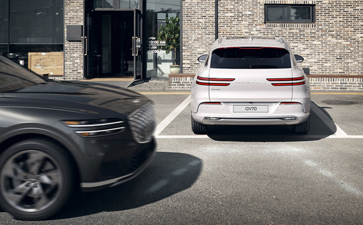  The Electrified GV70 reverses in the direction of a passing car with white lines depicting Reverse Parking Collision Avoidance Assist.
