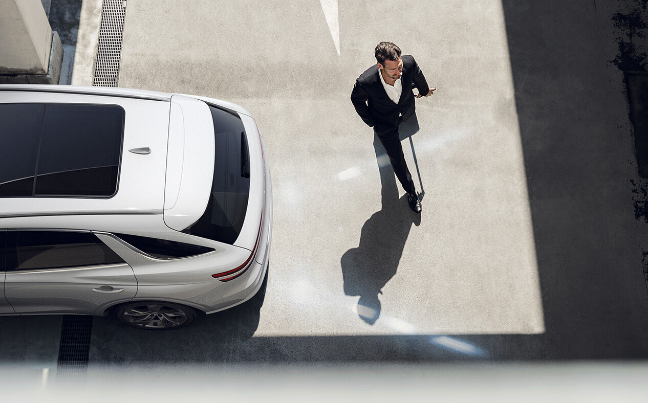 An aerial view of the Electrified GV70 reversing in the direction of a person crossing the street with white lines from the car depicting Reverse Parking Collision Avoidance Assist.