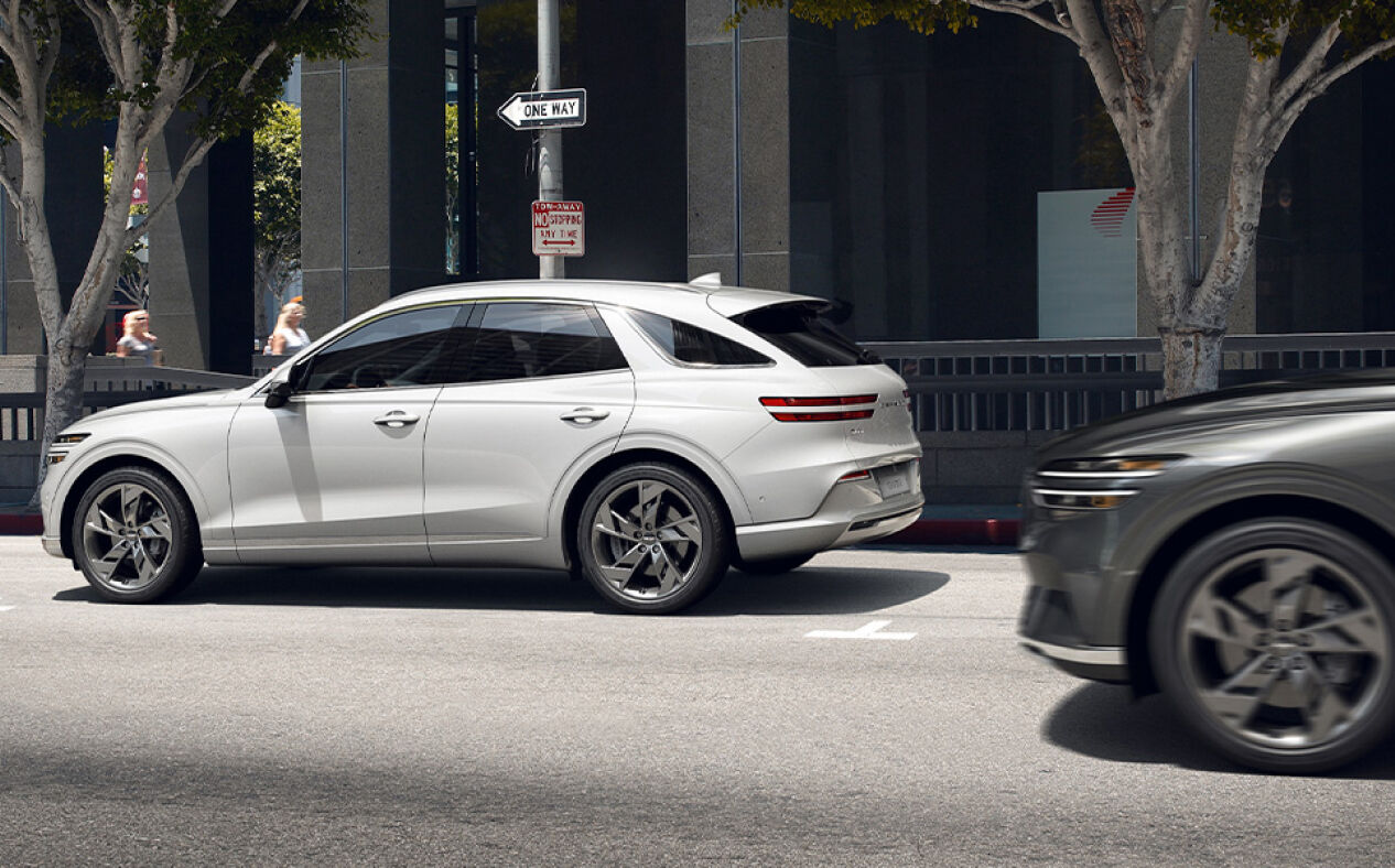 The Electrified GV70 is parked on the street as another car passes by from behind.