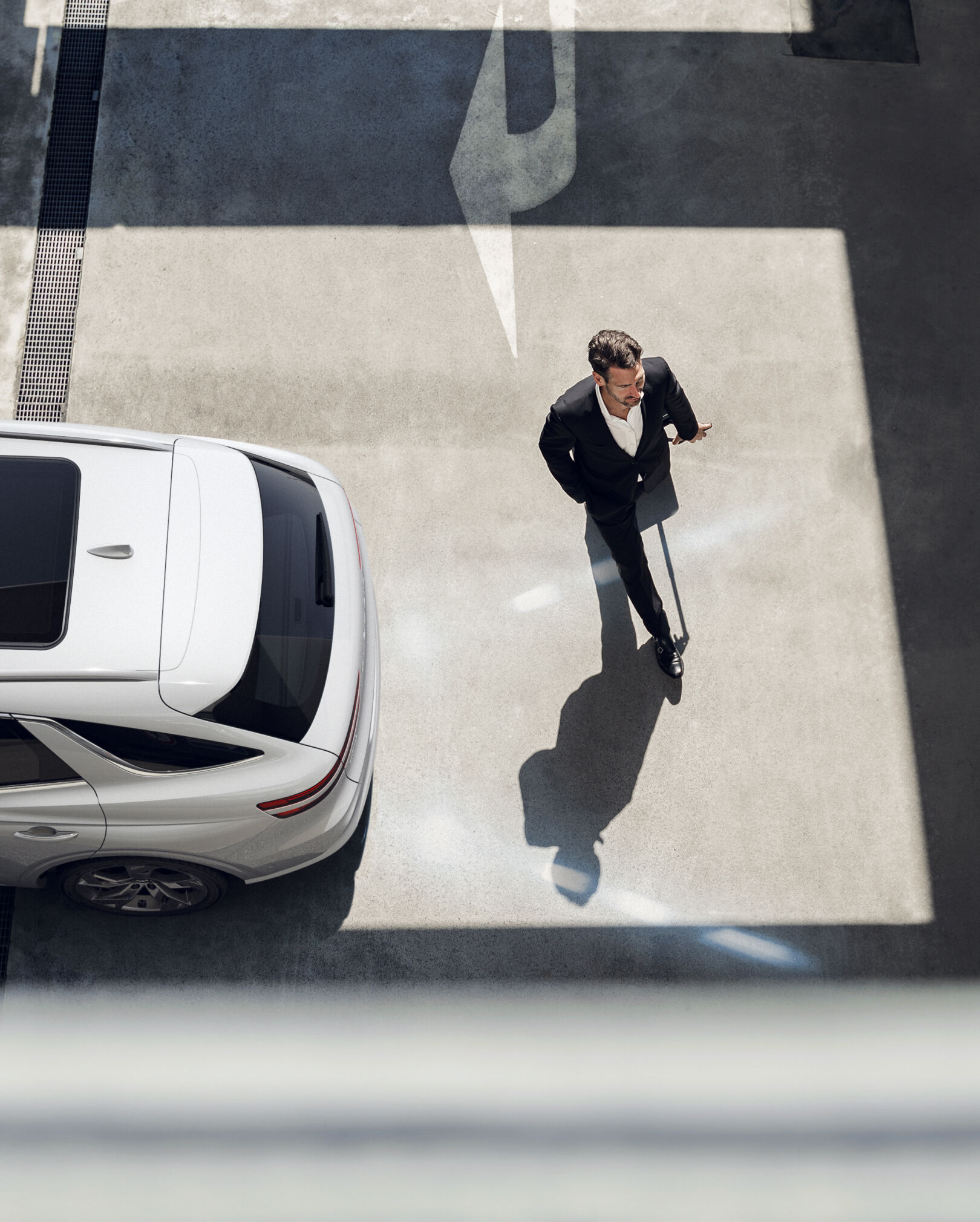 An aerial view of the Electrified GV70 reversing in the direction of a person crossing the street with white lines from the car depicting Reverse Parking Collision Avoidance Assist.