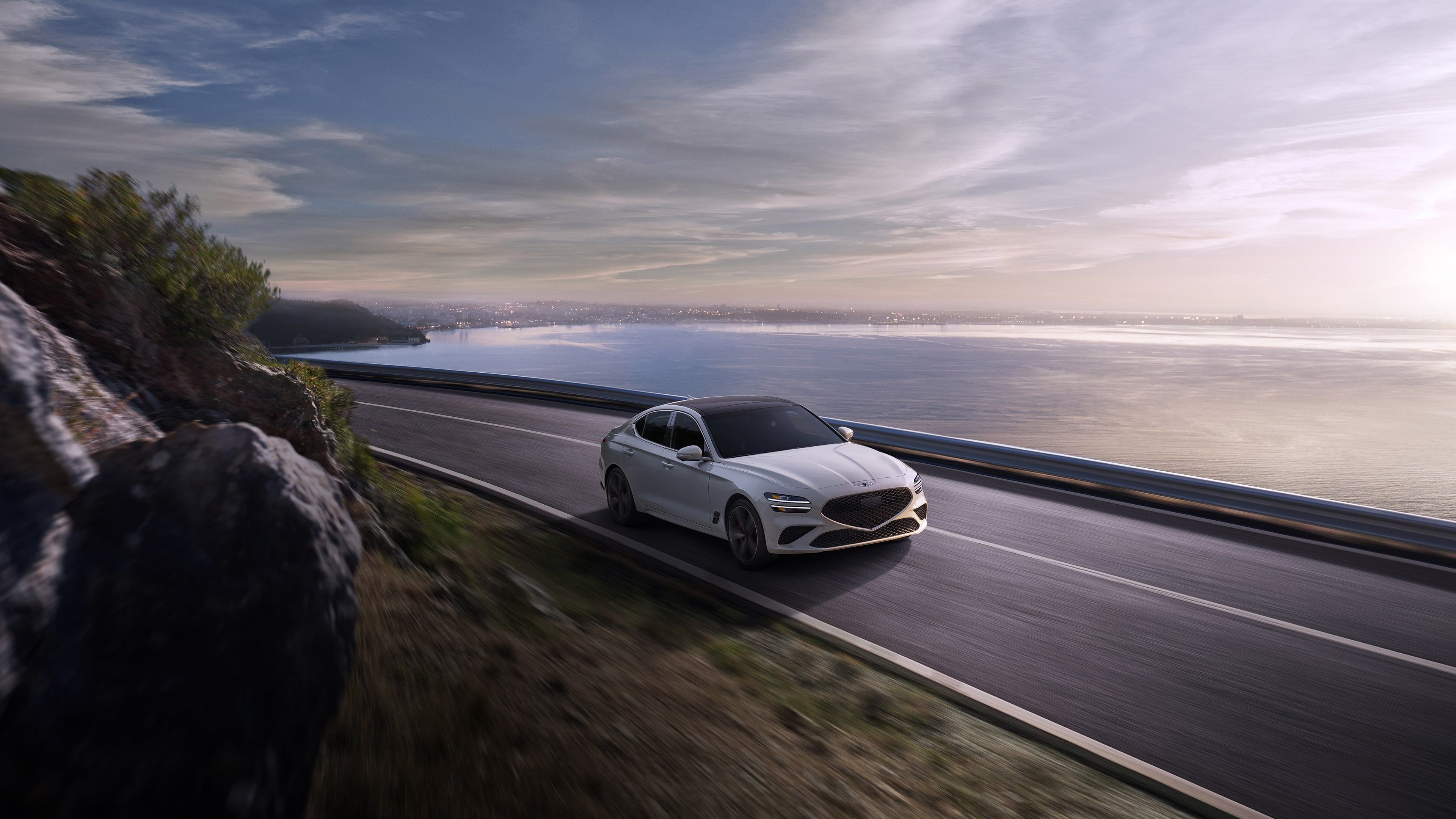 A white G70 driving around a bend on a coastal highway.