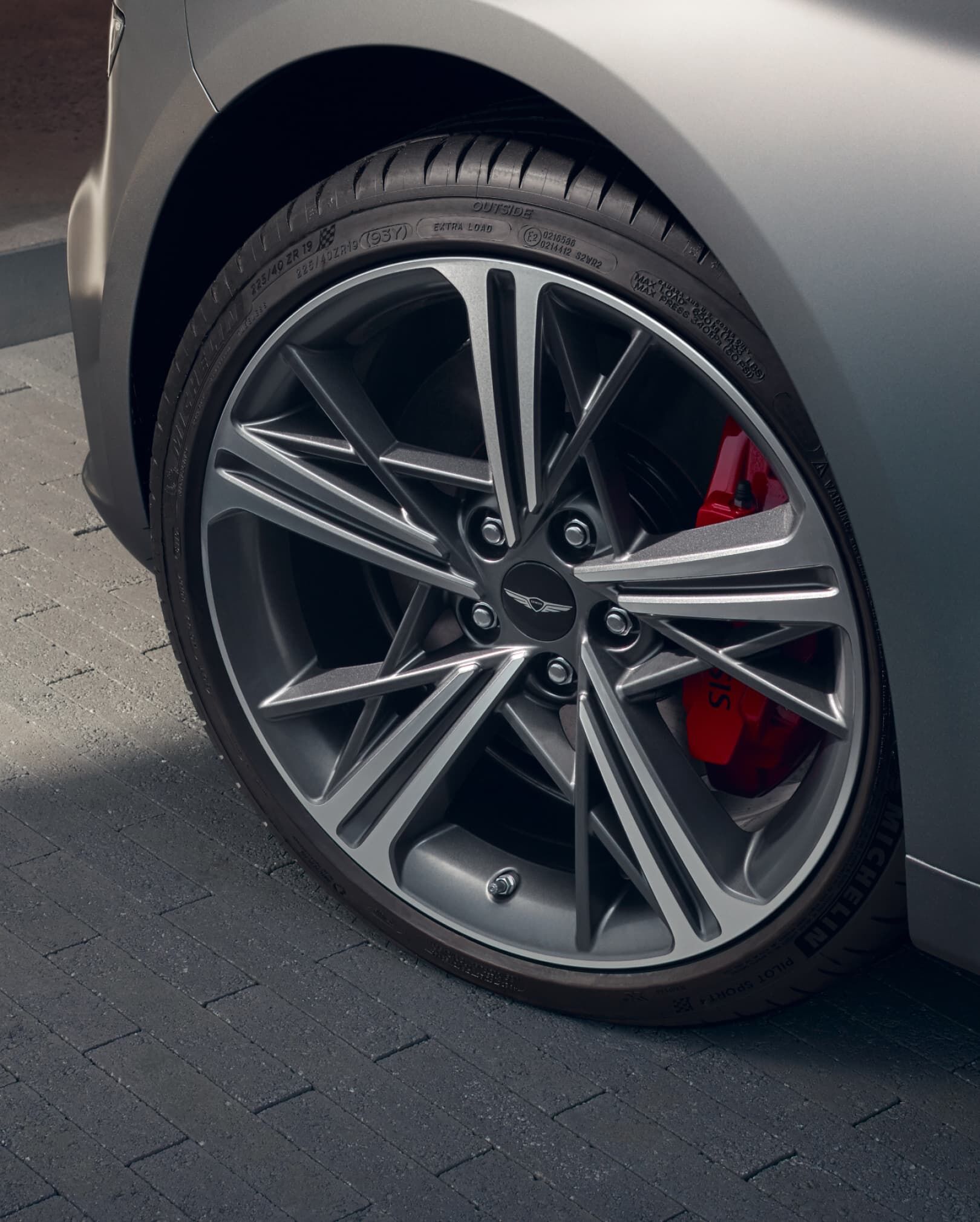 silver G70, closeup of front tire and red Brembo brakes