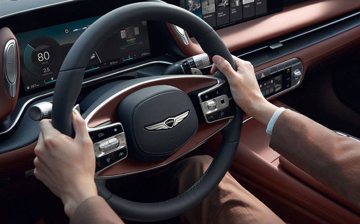 Hands hold the steering wheel in Bordeaux Brown interior.