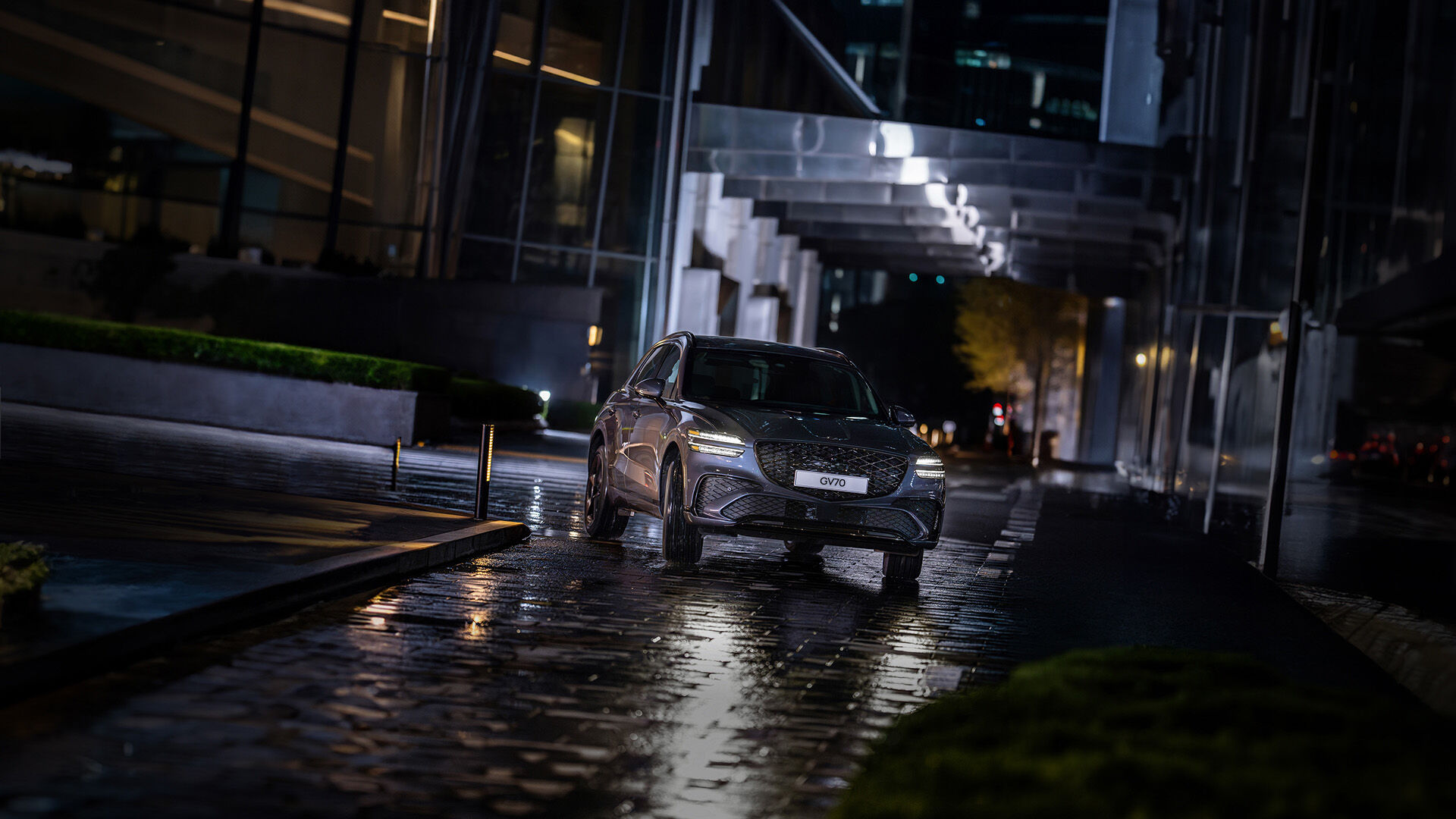 A Ceres Blue GV70 is parked in an outdoor space. The vehicle is facing forward with its headlights on.
