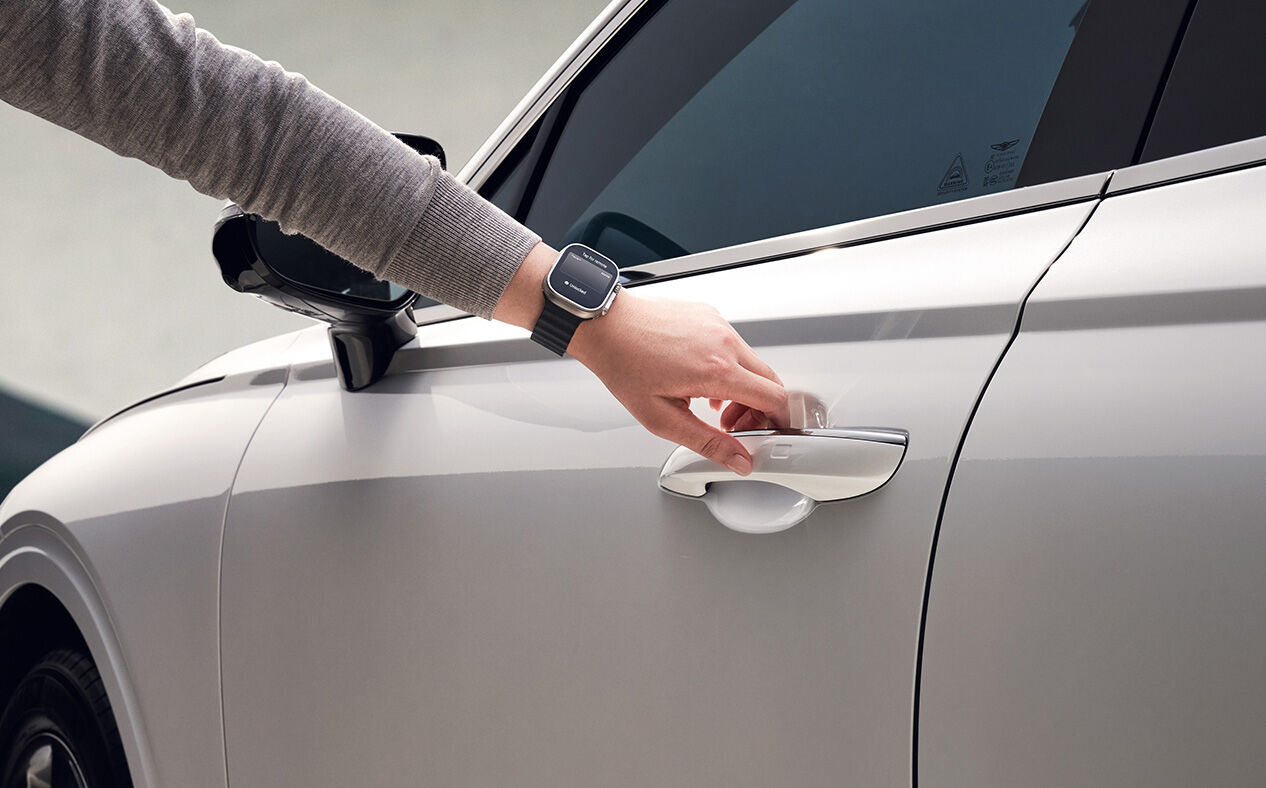 The driver is wearing a smartwatch running the MY GENESIS app and opening the door.