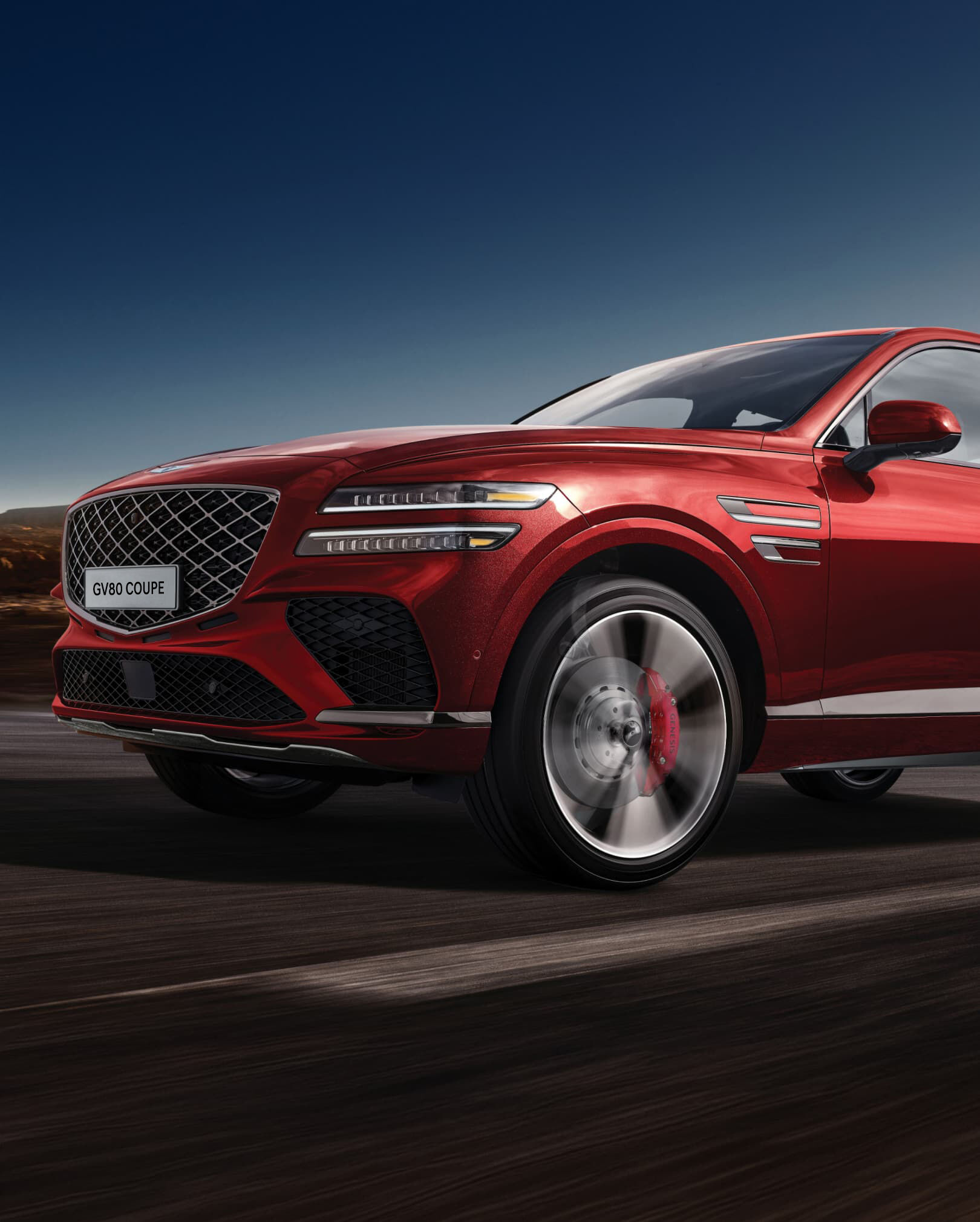 Gros plan sur le pneu côté conducteur du GV80 Coupé en Rouge Mauna, alors qu'il roule à vive allure.