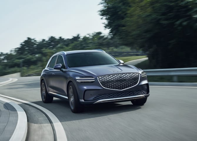 아스팔트 도로 위를 GV70 차량이 주행하고 있습니다. 