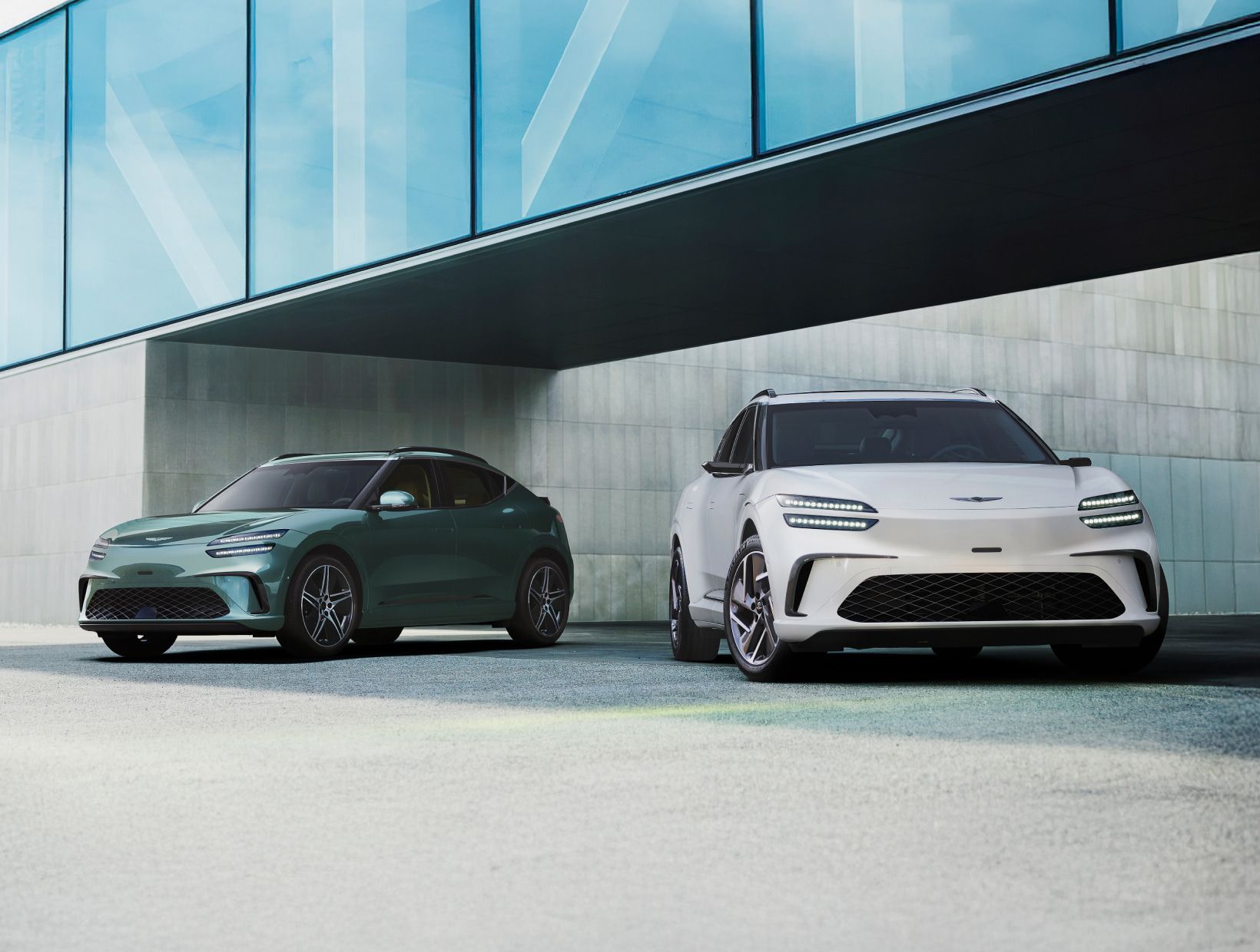 푸른색 통창이 보이는 건물 아래로 정차된 두 대의 GV60 차량이 보입니다.