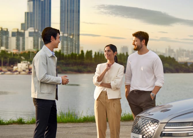 노을이 지는 빌딩과 강을 배경으로 남자가 두 남녀와 대화하고 있으며, 그 옆으로 Electrified G80 차량이 보입니다.