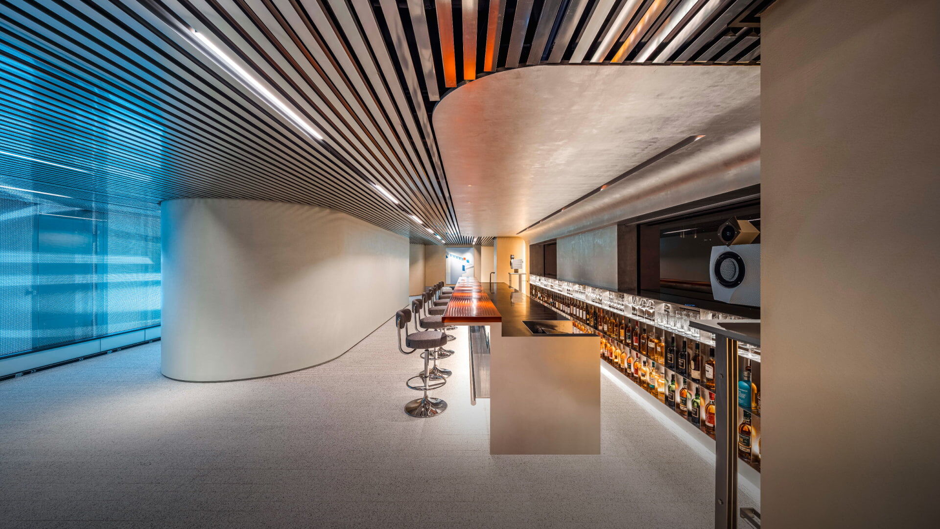 A side view of a whiskey and wine bar interior, where curved and linear ceiling designs blend harmoniously within an elegant, upscale ambiance.