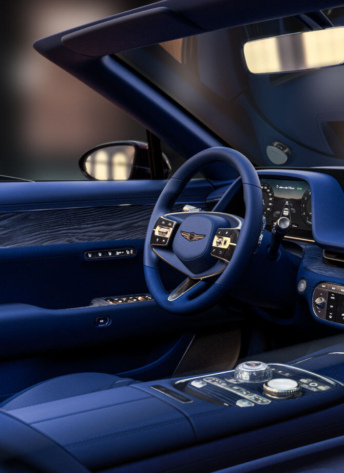 This is the interior driver's seat of the Genesis X Gran Convertible made of eucalyptus wood material. The steering wheel and controllers appear zoomed in.