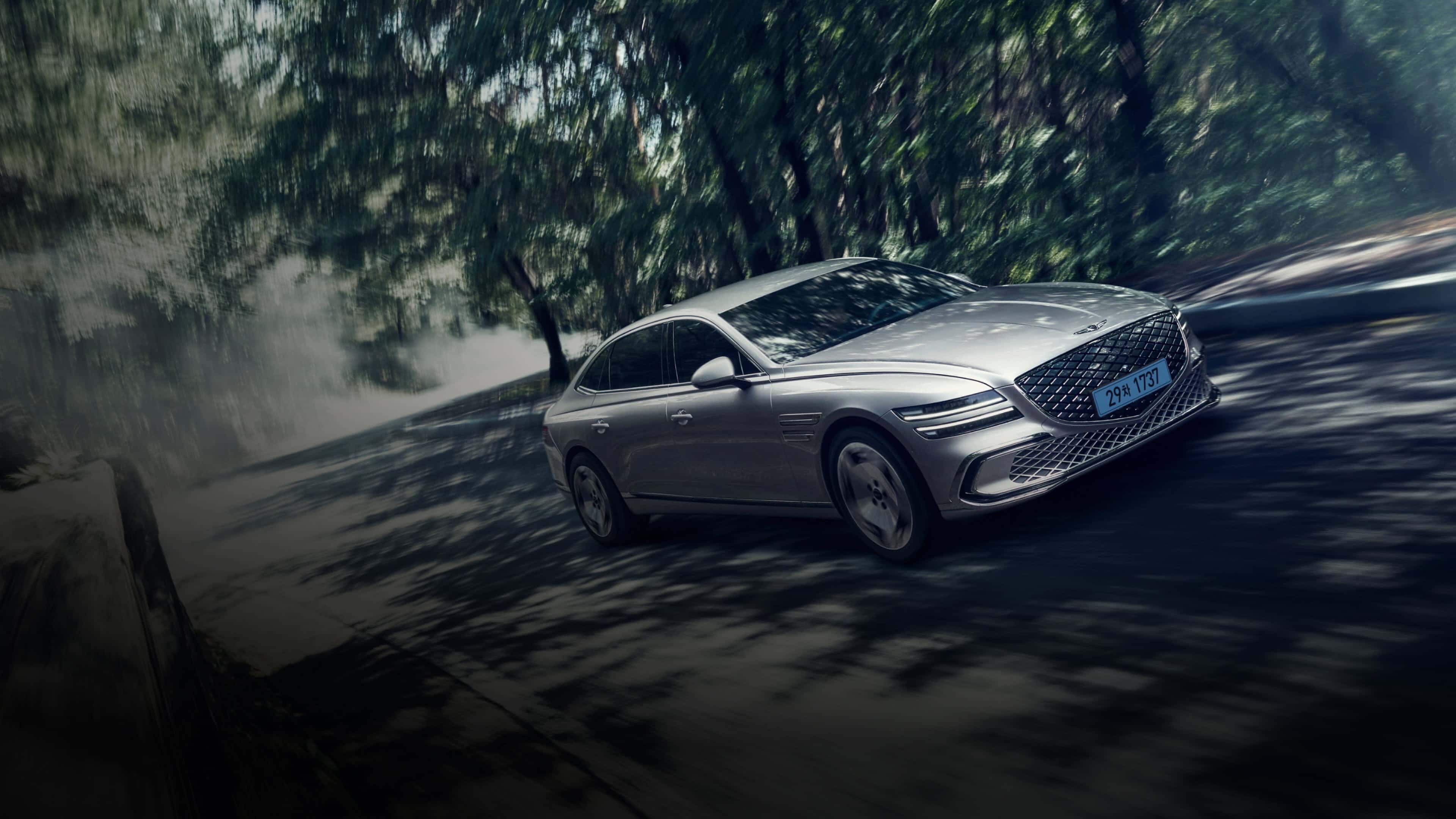 An Electric G80 is driving down a road lined with leafy trees on both sides. The dynamic ride is evident in the swaying of the landscape as the vehicle passes by.