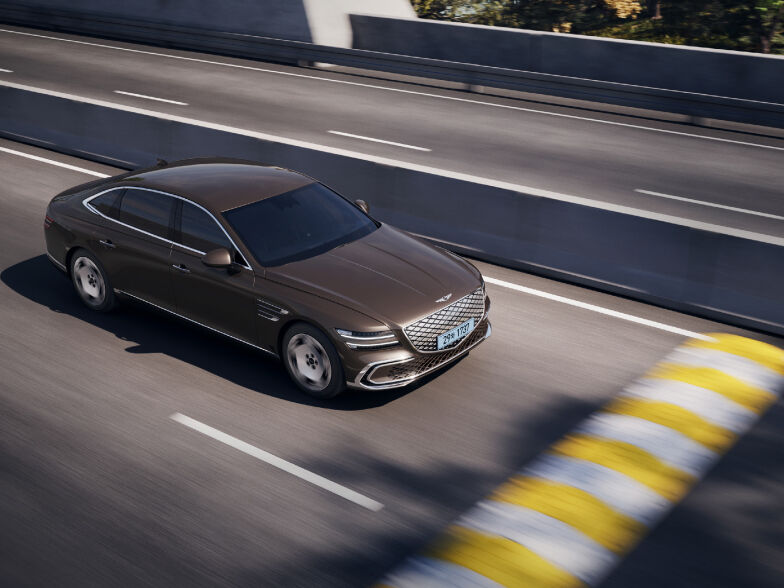 An Electrified G80 is driving down the road. A speed bump is placed in front of the vehicle.