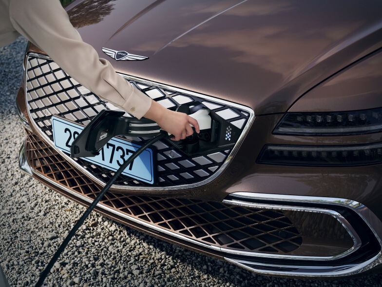The charge door located on the front crest grille of the Electrified G80 is open and the charge nozzle is plugged in.