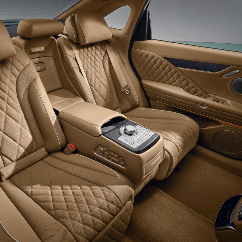 View of the back seat inside the Electrified G80. The quilted seats in a luxurious ecru camel monotone and the controller in the center are visible.