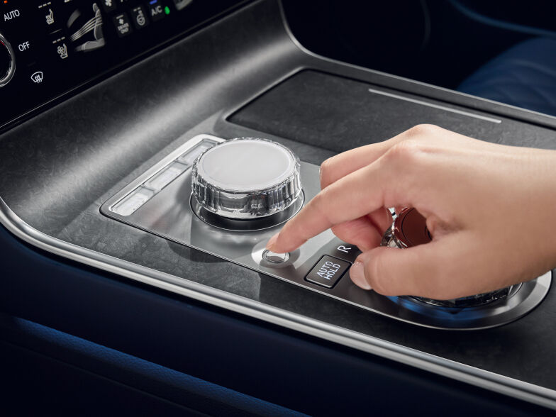 The center control panel, located between the driver and passenger seats, is visible. A hand is seen trying to press the integrated controller.