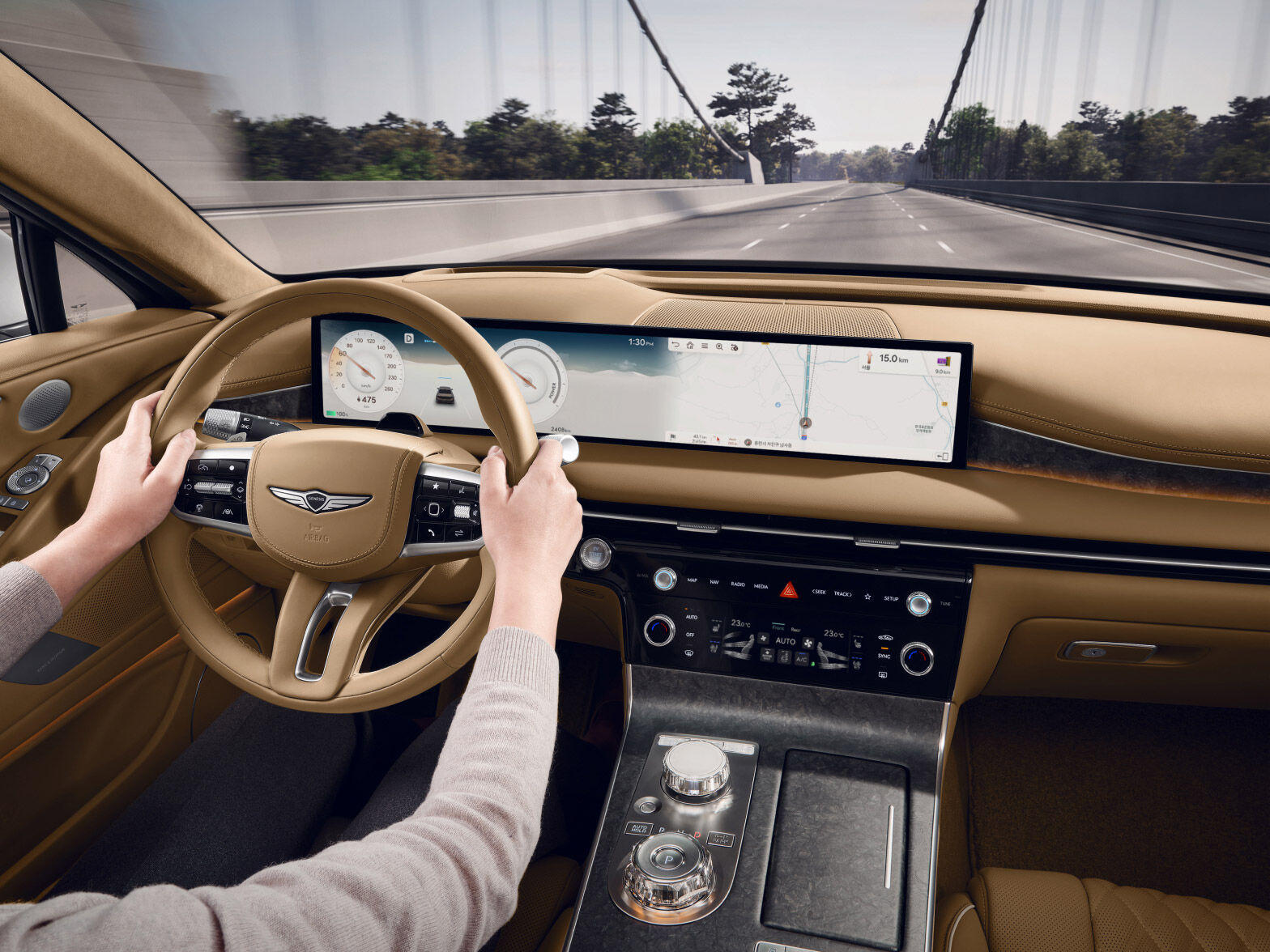 A full view of the front of the front seat. Two hands holding the steering wheel, the panoramic display, and the center fascia are shown.