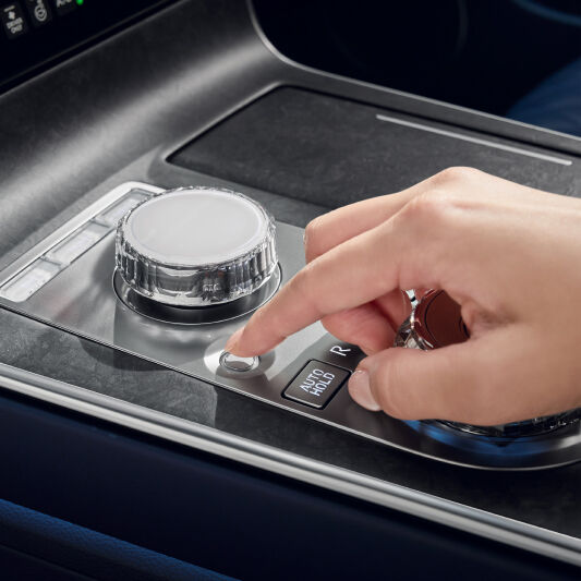 A view of the center control panel, located between the driver and passenger seats, is visible. A hand is seen trying to press the integrated controller.