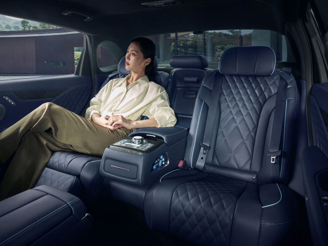 A young woman is sitting in the rear VIP seat of an Electrified G80. Notice the leg rests for her legs to rest comfortably and the armrests for her arms to rest comfortably.