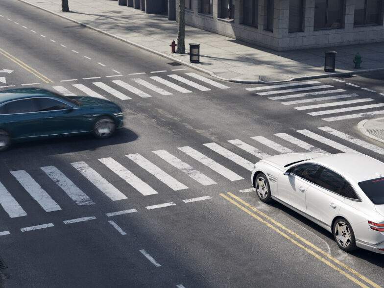A glossy Uyuni White Electrified G80 waiting to pass through an intersection and another vehicle about to pass in front of it.