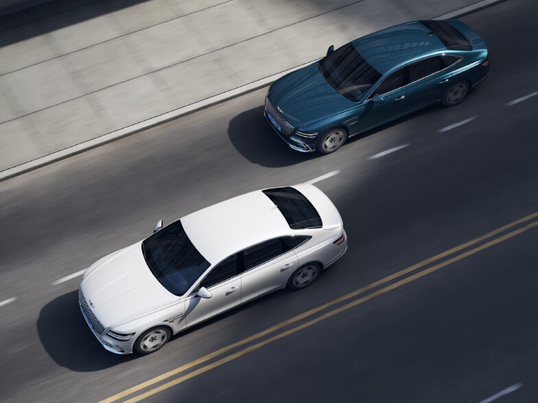 Two Electrified G80s are traveling on a two-lane road. The car driving in the first lane is ahead, and the car driving in the second lane is behind.