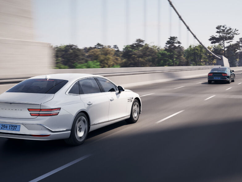 Two vehicles are traveling on a road. An Electrified G80 is seen driving away from the vehicle ahead of it.