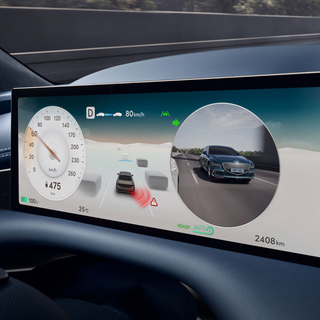 The display in front of the driver's seat shows dashboard graphics, a view of the vehicle from the outside, and a view of the vehicle from behind driving on the road.