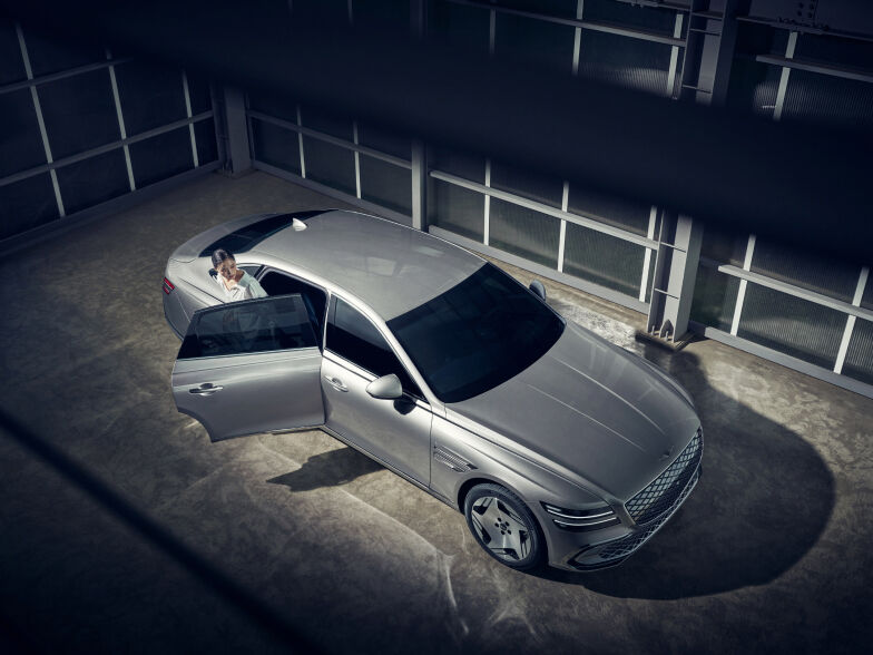 A woman is getting out of the back seat of an Electrified G80 that is parked in an interior space.