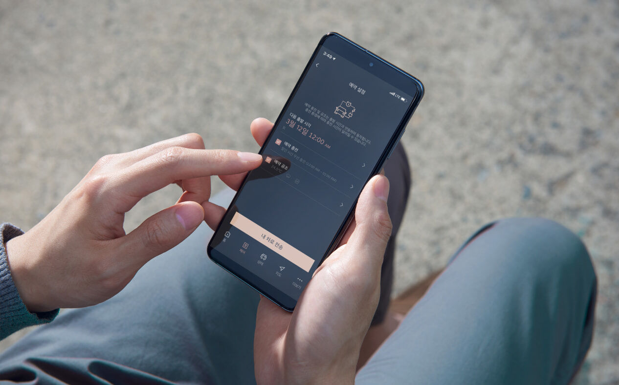 A hand holding a smartphone and using the Genesis dedicated app to set up reserved charging.