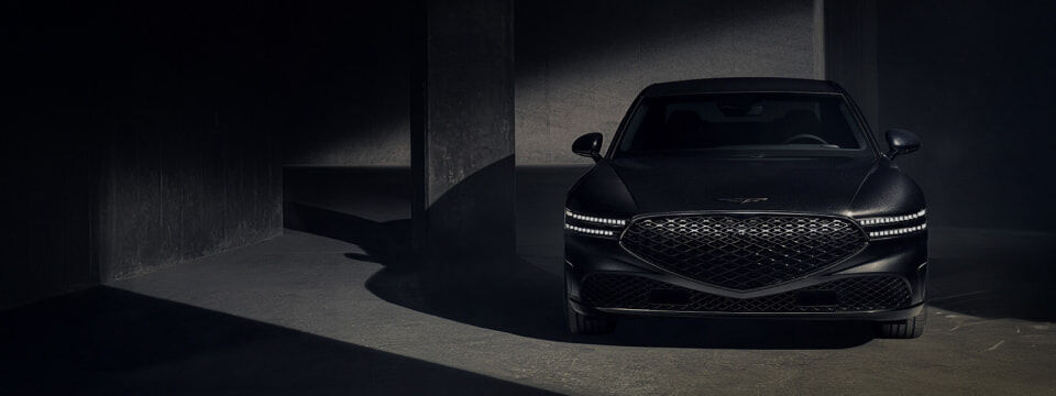 The G90 Black is parked in a dark space with its headlights on, facing forward.
