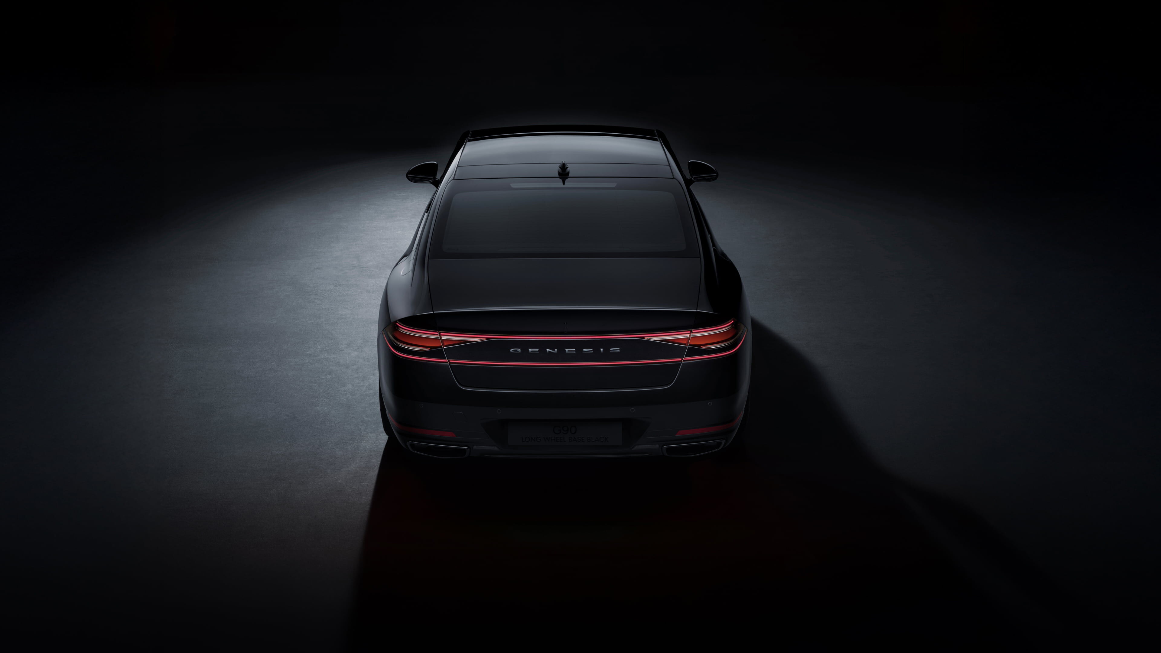 A rear view of the G90 Long Wheel Base Black, parked on illuminated ground in a dark space.