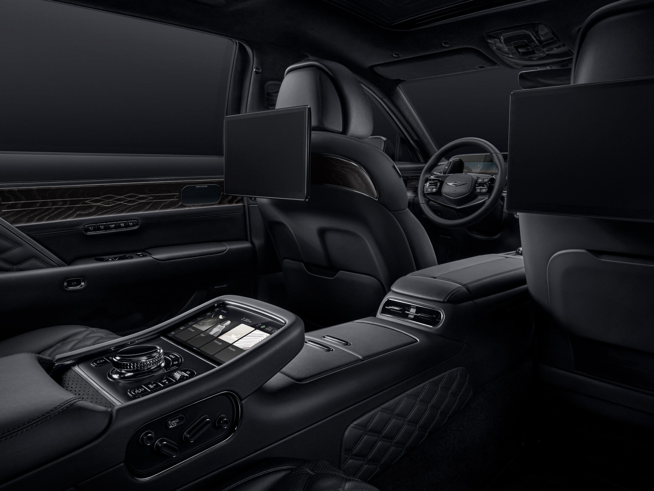 The rear seat interior of the G90 Long Wheel Base Black unfolds from the perspective of the rear seat, looking toward the driver’s seat. The power-operated rear smart entertainment system and center console are visible, with all elements finished in black.