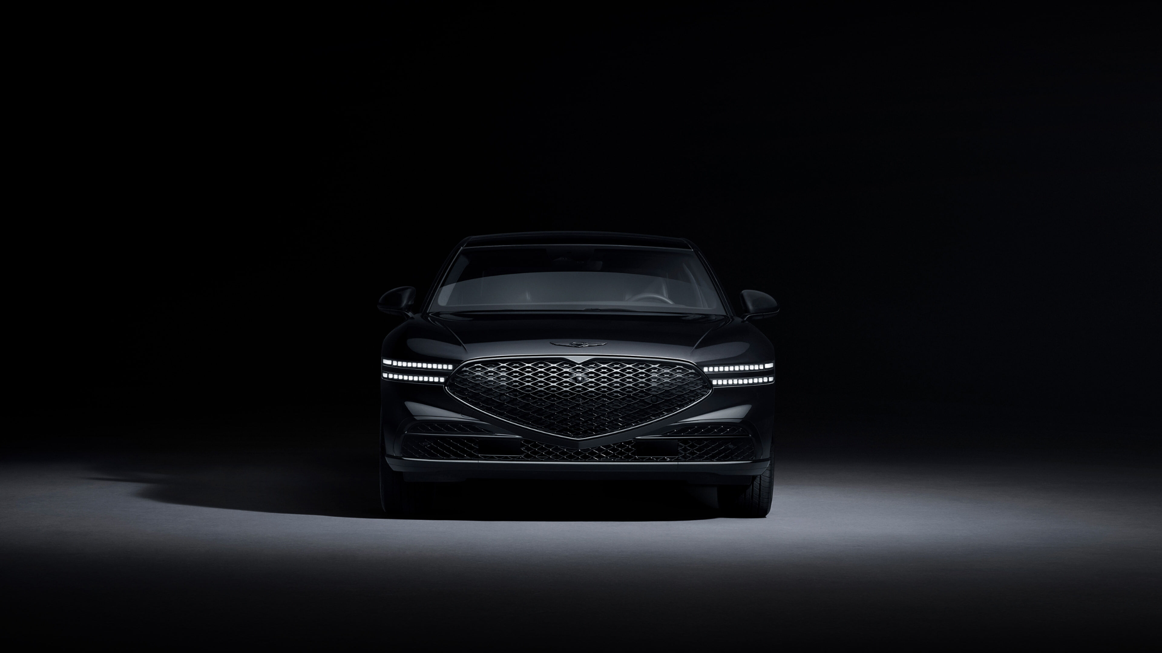 A front view of the G90 Long Wheel Base Black, parked on illuminated ground in a dark space..
