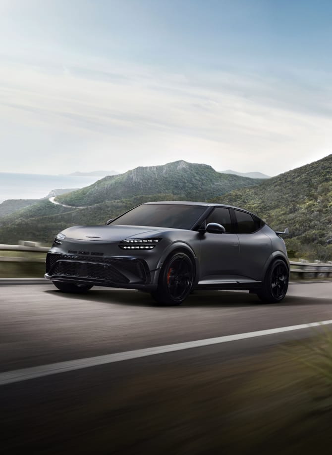 산맥을 배경으로 고속도로를 주행하는 정측면의 마칼루 그레이 색상의 GV60 Magma 차량 이미지입니다.