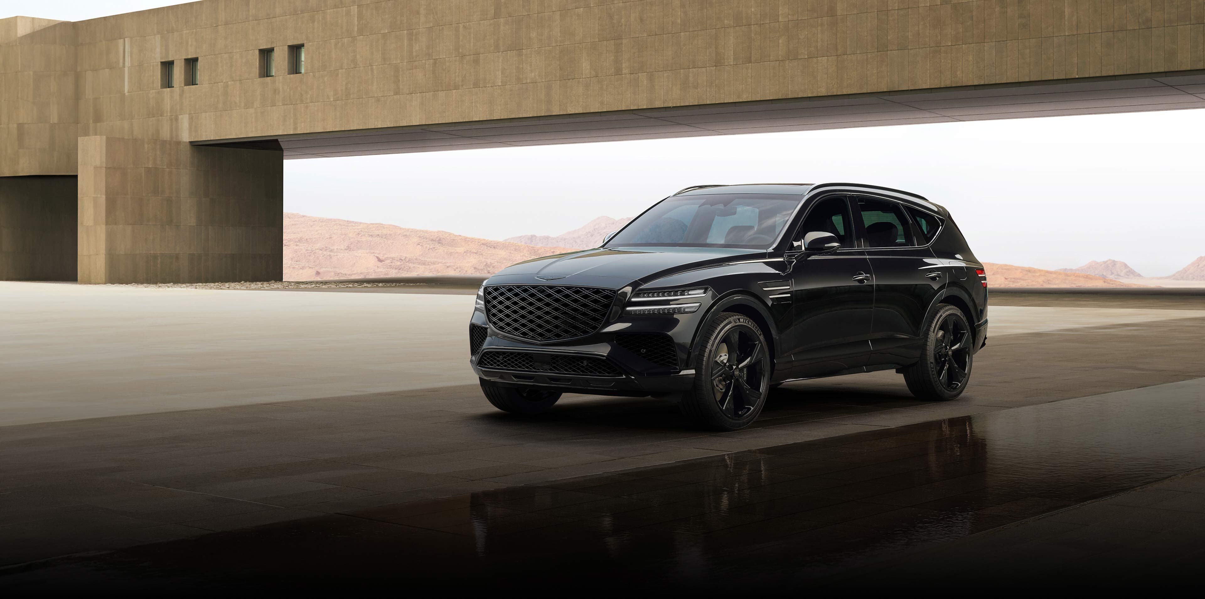 The GV80 Black is seen parked diagonally in front of a brown building against a desert background.