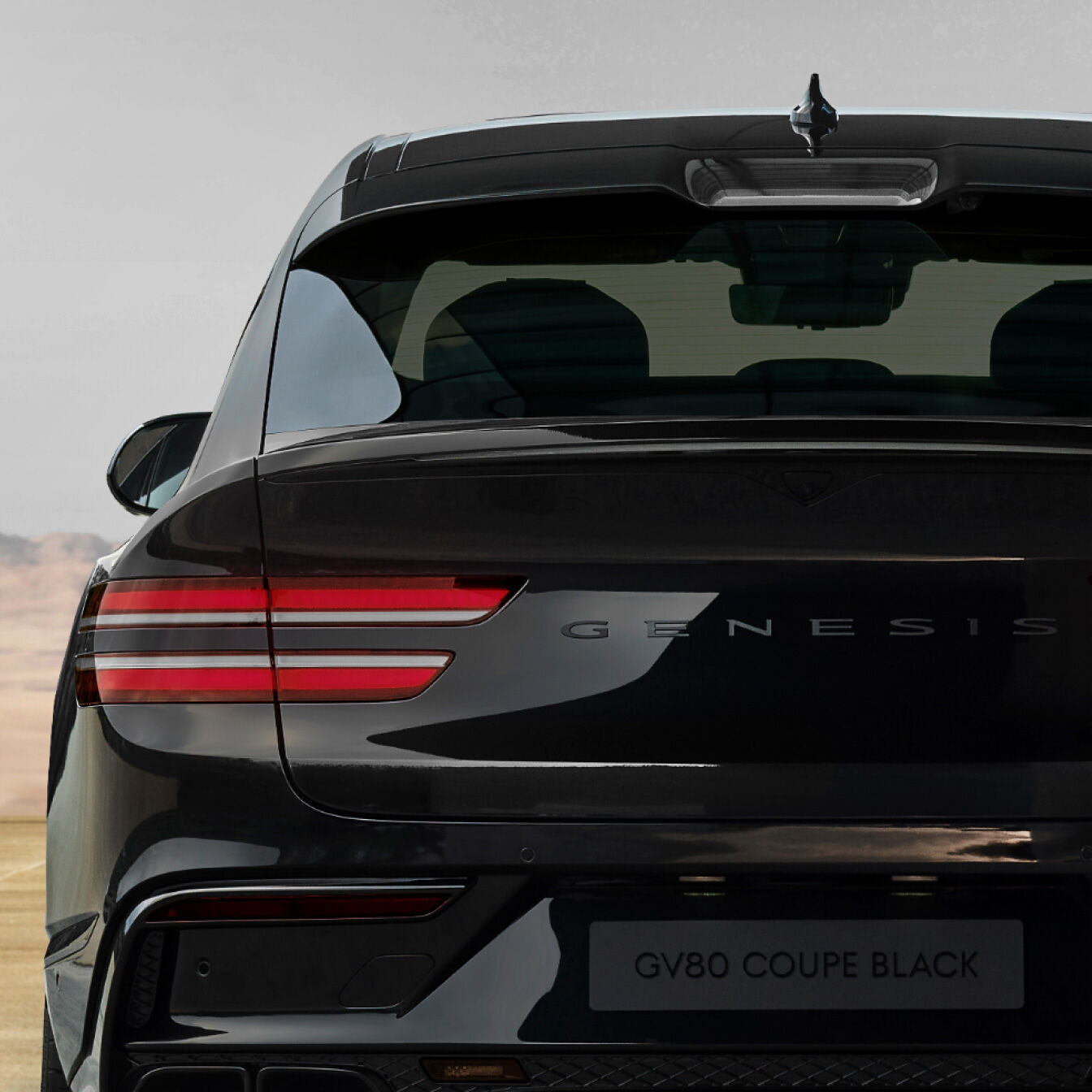 At the rear of the GV80 Coupe Black, the metallic lettering that spells 'GENESIS' is visible. Two red light strips are illuminated.