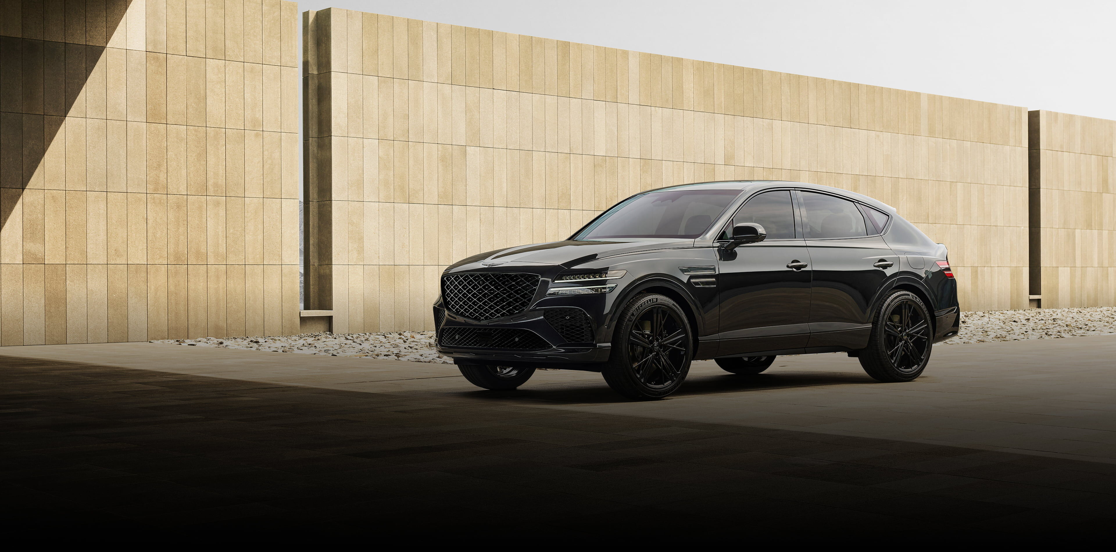 The GV80 Coupe Black is parked diagonally in front of a high wall made of brown tiles.