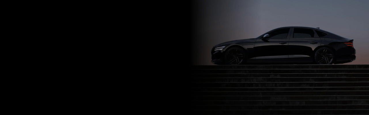 계단 위의 공터에 G80 Black이 좌측면을 보이며 서 있습니다. 차량의 부드러운 측면 라인이 강조되어 보입니다. 그 뒤로 저녁 무렵의 노을에 물든 보랏빛의 하늘이 펼쳐져 있습니다.