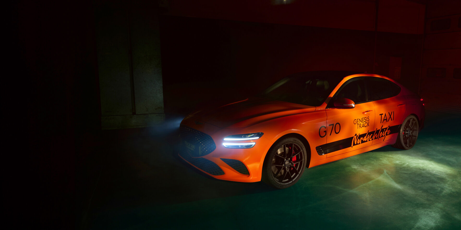 The G70 Track Taxi Nordschleife is parked within darkness, with only its headlights on.