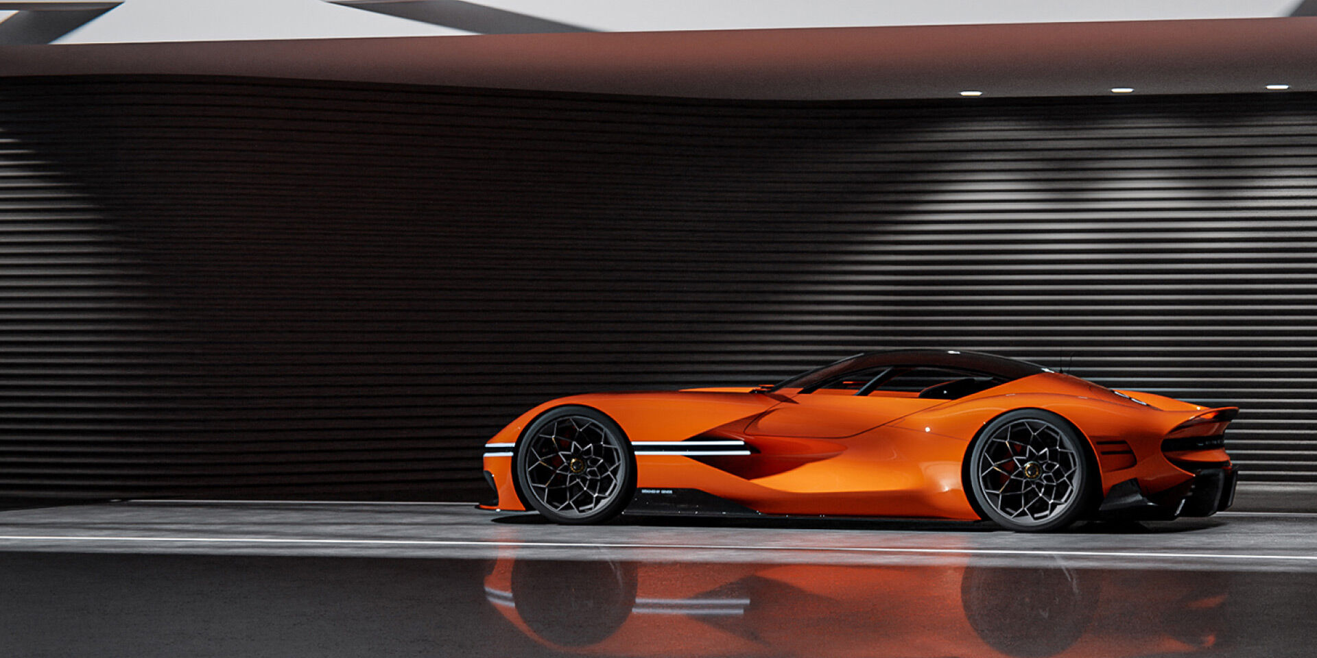 The X Gran Berlinetta Concept stands poised in front of a dark panel wall, illuminated by white overhead lights. Its side profile and lit headlamps reflect elegantly off the sleek, glossy floor.