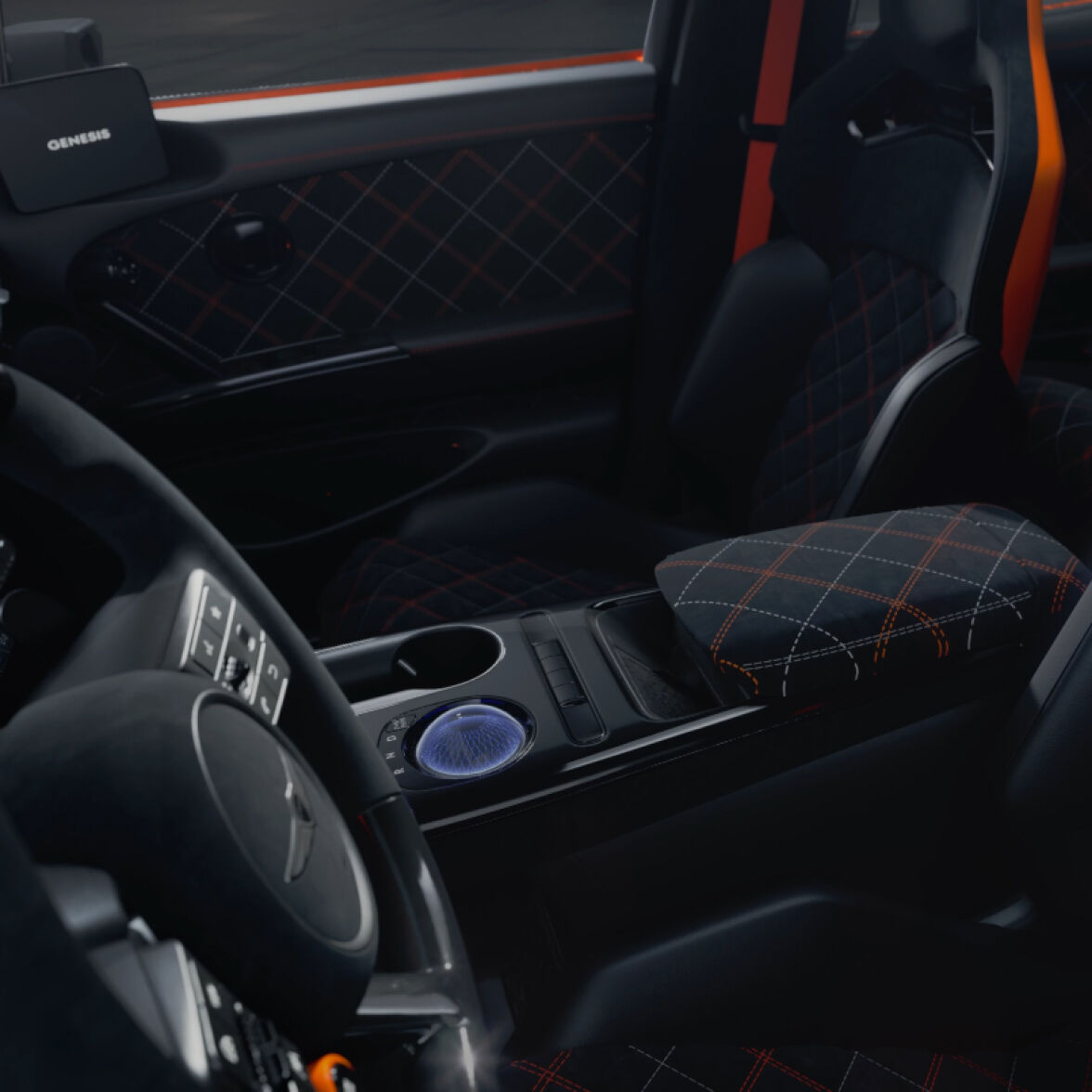 The steering wheel of the GV60 Magma is shown, with eye-catching orange buttons on both sides symbolizing magma. In the background, a long display screen is visible.