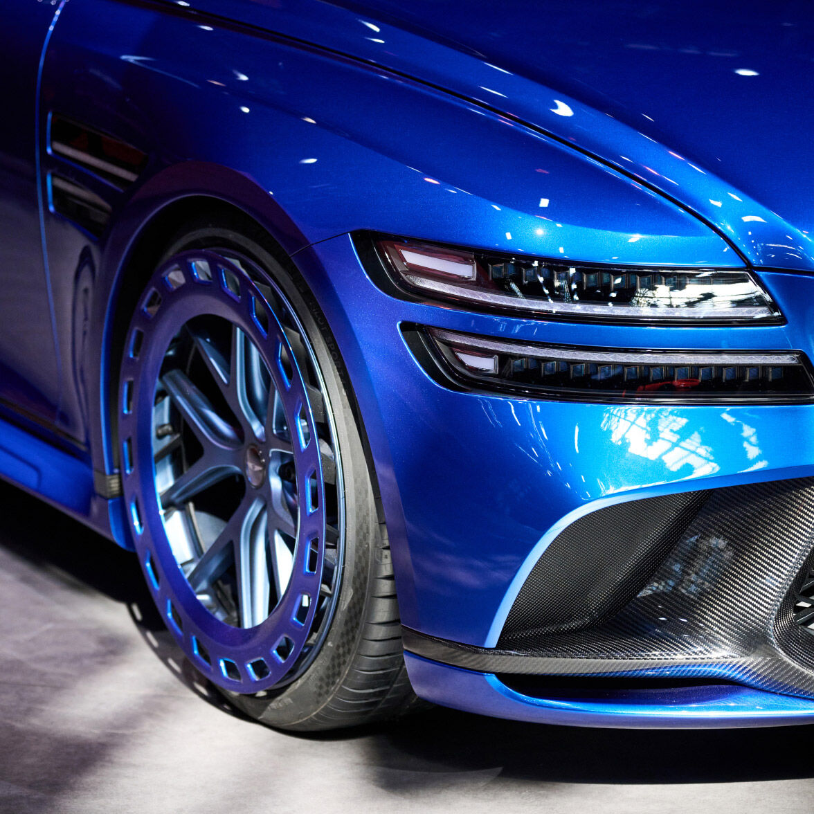 Vision blue and acme blue two-tone Genesis G80 EV Magma Concept's wheels and front bumper can be seen.