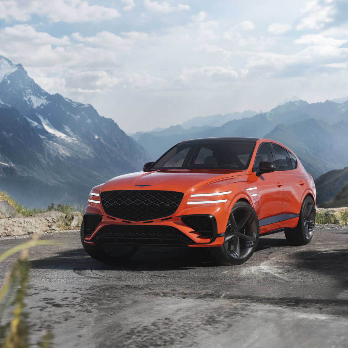 The GV80 Coupe Concept is parked outdoors with its white headlights on, facing forward. A vast mountain range stretches out in the background.