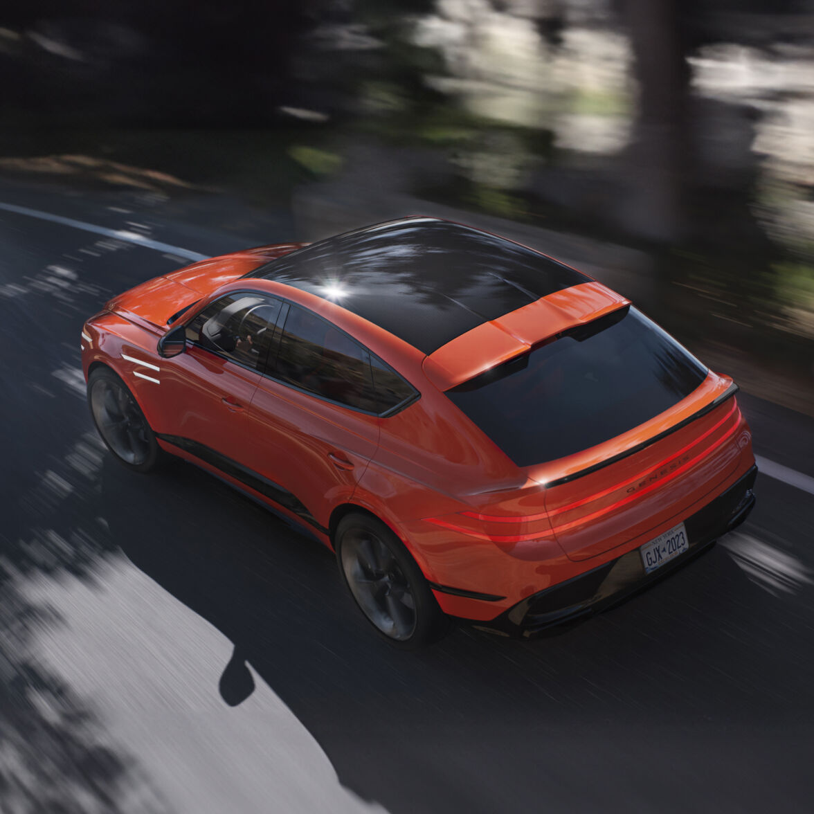 A diagonal overhead view shows the rear of the GV80 Coupe Concept as it speeds down the road.