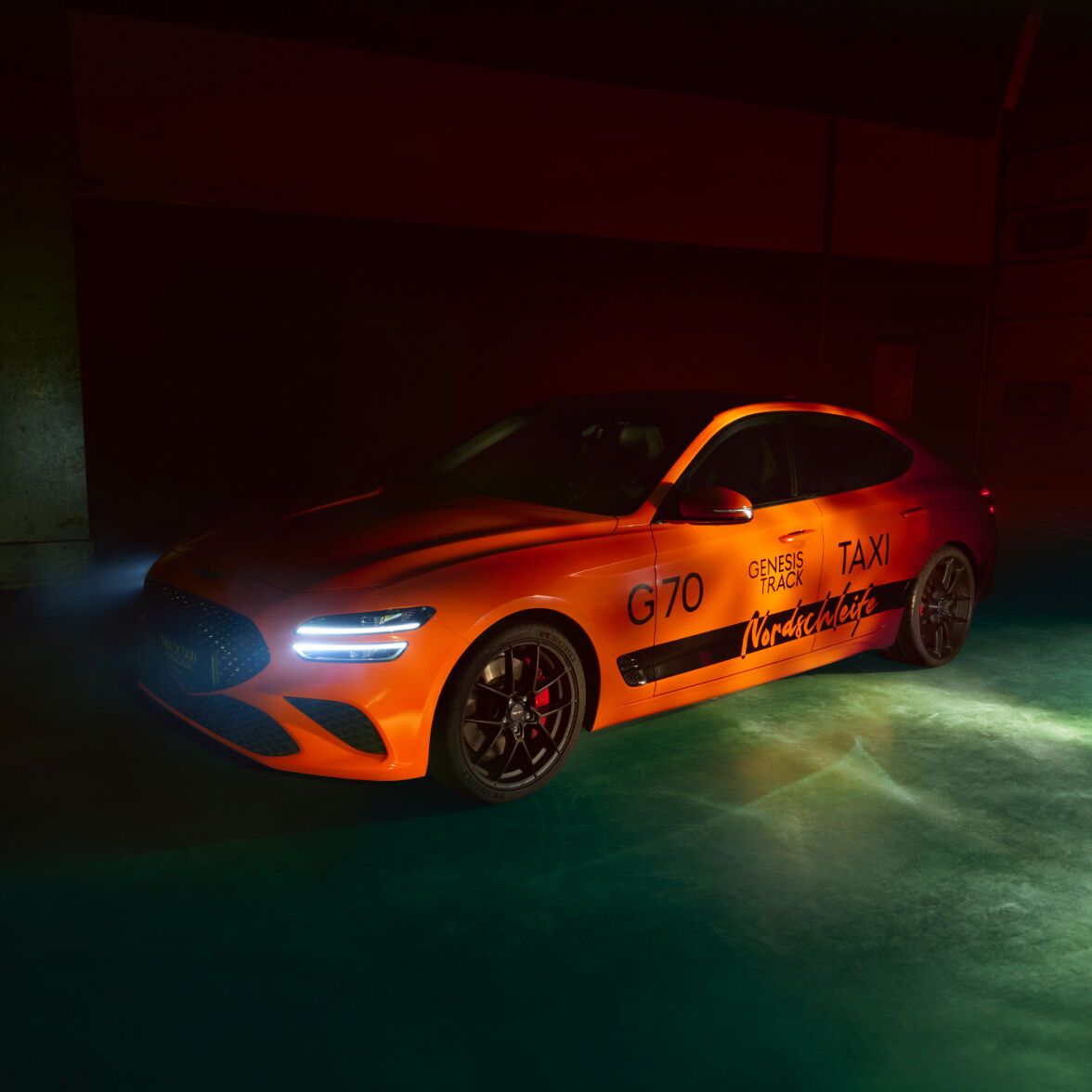 The Track Taxi G70 is parked within darkness, with only its headlights on.