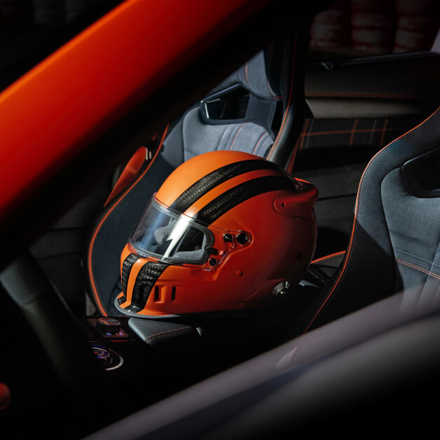 On the right side of the screen, an image shows the interior of a magma-colored vehicle. Viewed from the driver's seat, an orange racing helmet is placed on the passenger seat. 