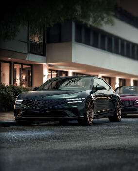 Genesis X Gran Coupe and Convertible concept vehicles are parked in front of a dark, luxurious background. At the front, the LED lights and signature grill stand out, and at the back, a convertible model with an open roof is visible.